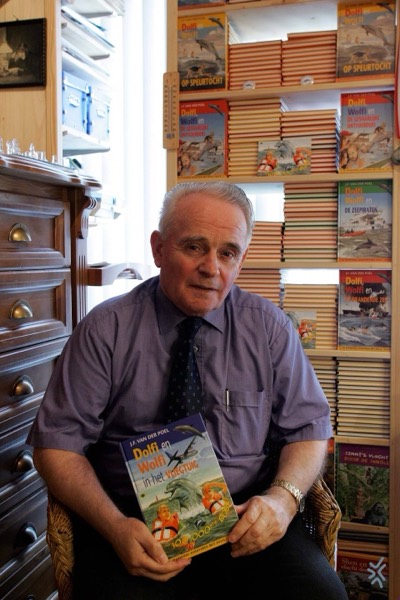 J.F. van der Poel met een deel van Dolfi en Wolfi in zijn handen, voor een kast vol boeken uit de serie.